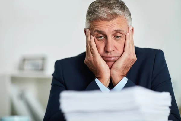 Another day, another pile of paperwork. a mature businessman looking at paperwork and feeling overwhelmed