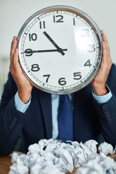 Running out of time. an unrecognizable businessman holding a large clock in front of his face
