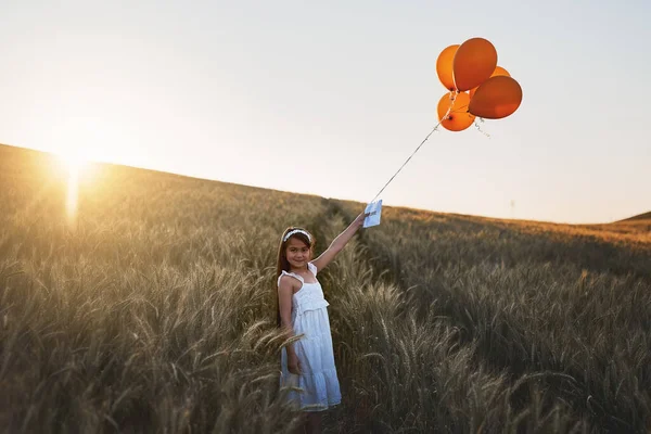 Letters from heaven. a cute little girl attaching a letter to a bunch of balloons while standing in a cornfield