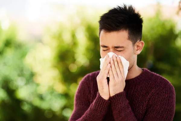 He just cant stop sneezing. a young man blowing his nose outside