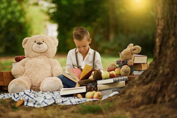 Books are a uniquely portable magic. a little boy reading to his toys while out in the woods