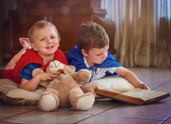 Sparking their imaginations at story time. Portrait of a happy little boy listening to his brother read a story while they lie on the floor at home