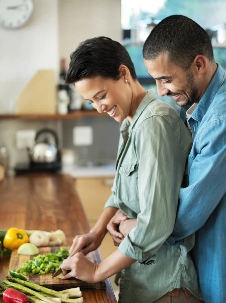 Need a hand...an affectionate young couple preparing a meal together in their kitchen