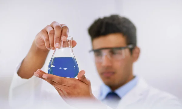 Finding cures in the lab. a lab technician examining a beaker of blue liquid while standing in a lab