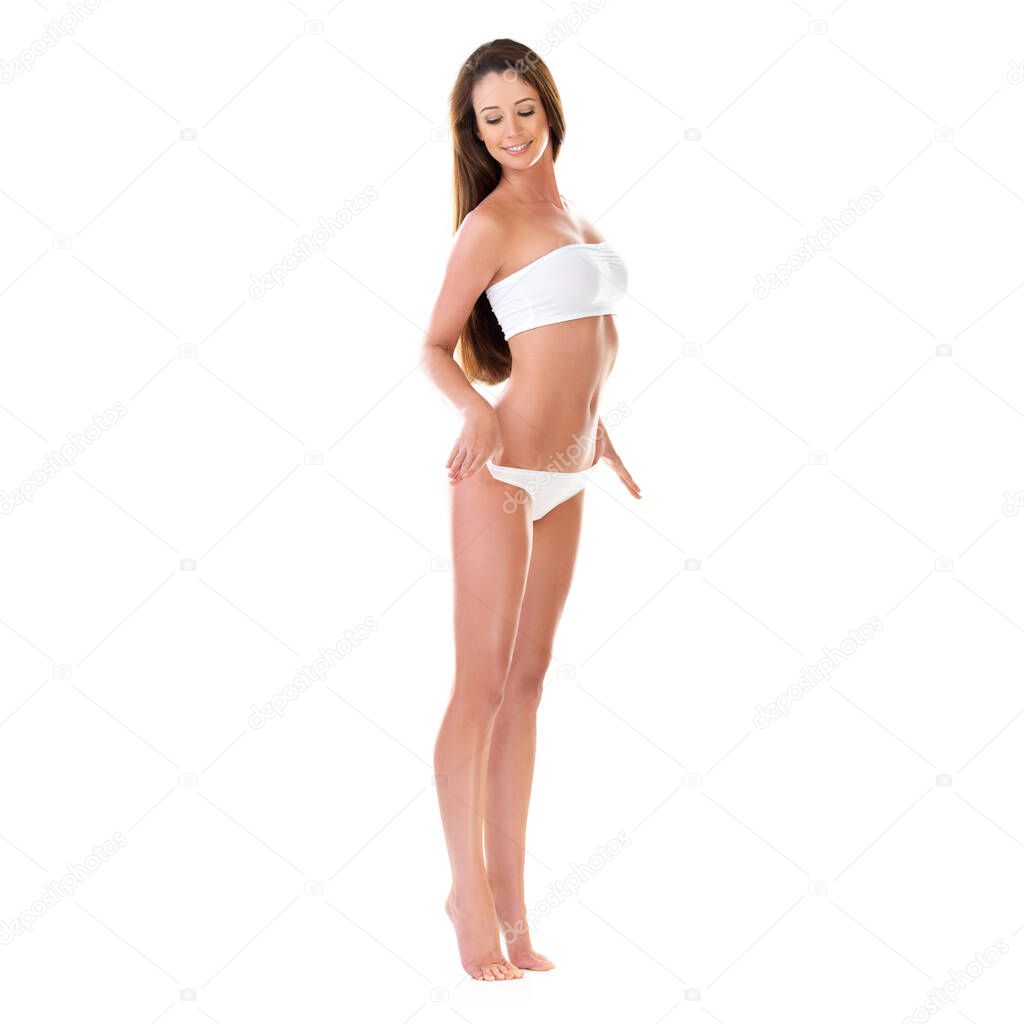She makes that bikini look even better. Studio shot of a beautiful young brunette woman in a white bikini pulling on her waistband isolated on white