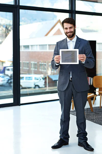 Take a look at how well business has been improving. Portrait of a young businessman holding up a digital tablet in front of him in a modern office