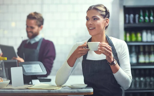 This coffee is definitely going on the menu. a young woman having coffee in her store while her coworker uses a digital tablet in the background