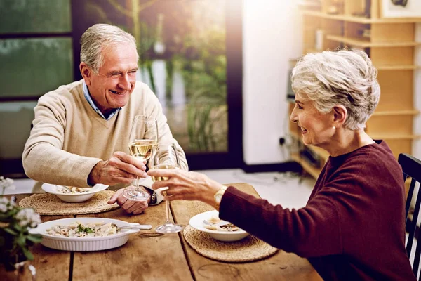 May we have many more years together. an elderly couple toasting with wine glasses while they enjoy a meal at home