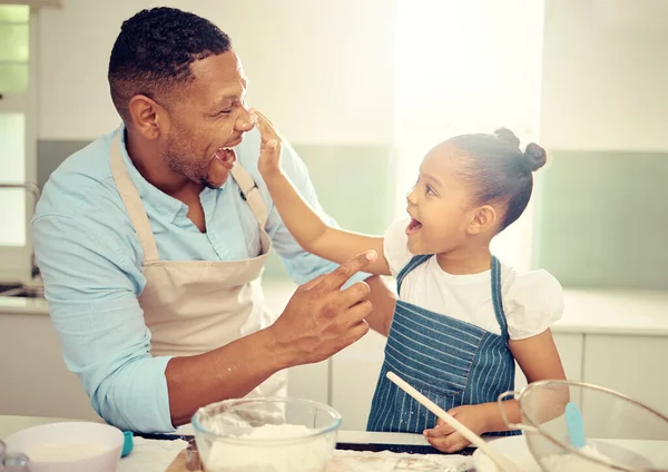 Father, playing and girl baking in family kitchen with flour, food and dough while learning to bake cake. Happy dad teaching playful daughter cookies recipe with excited young kid helping at home.