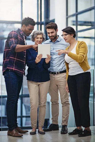 That looks interesting. a group of colleagues looking at a tablet in the office