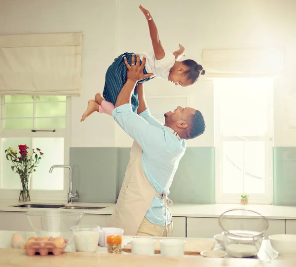 Happy black father and daughter playing in a kitchen while cooking together, bonding and laughing. African American parent enjoying family time with his child, playful and having fun while baking.