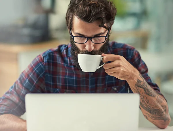 One sip of coffee does wonders for my creativity. a designer having coffee while working on his laptop
