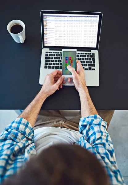 Moving closer to business goals with the help of technology. High angle shot of a young designer using a cellphone in a modern office