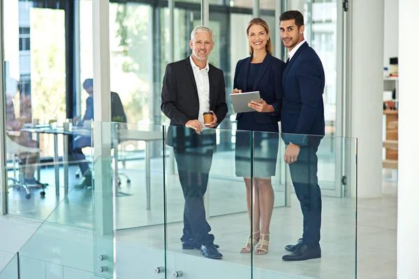 Were bringing the future of the company closer. Full length portrait of a group of young businesspeople standing together in a modern office and using a tablet