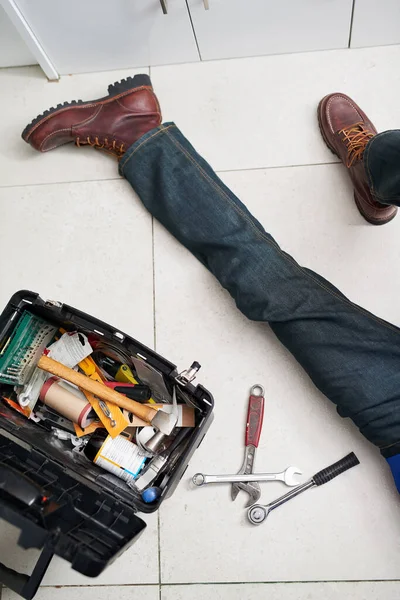 Hes got the tools to tend to your plumbing requirements. a handyman conducting repairs on the floor next to his tool box