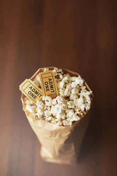 Movies arent the same without popcorn. a bag of popcorn and two movie tickets on a wooden background