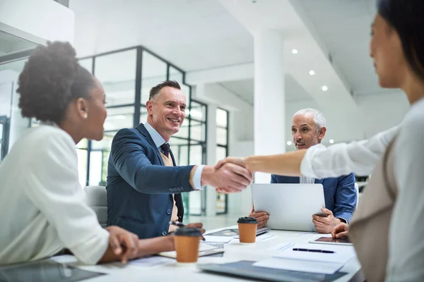 Extending a warm welcome to a new staff member. businesspeople shaking hands during a meeting in a modern office