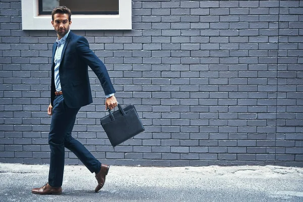 Every businessman needs a briefcase. a handsome young businessman carrying a briefcase against a grey facebrick wall