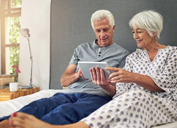 Lets plan an adventurous day online. a senior couple using a tablet while lying in bed