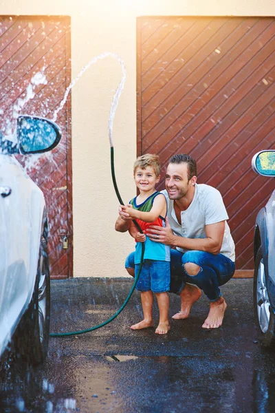 I love that dad includes me in the chores. Full length shot of a father and son playing with a hosepipe while washing a car together