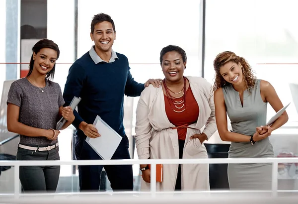 Were accomplishing our goals together. a young diverse group of colleagues standing together in the office and smiling at the camera