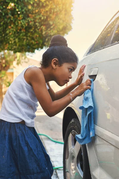 Making sure she doesnt miss a spot. a young girl busy cleaning a car outside