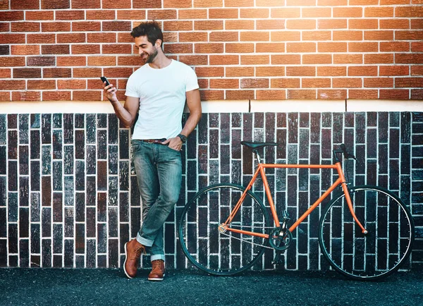 His city keeps him connected. a handsome young man standing next to his bicycle and using a phone in the city