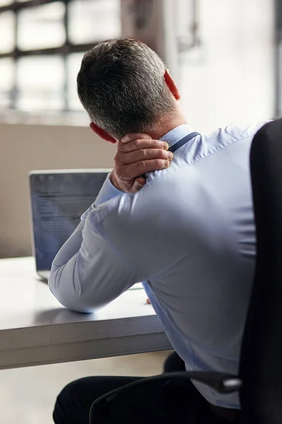 Hes been seated for too long. Rearview shot of a mature businessman running his neck anxiously while working in his office