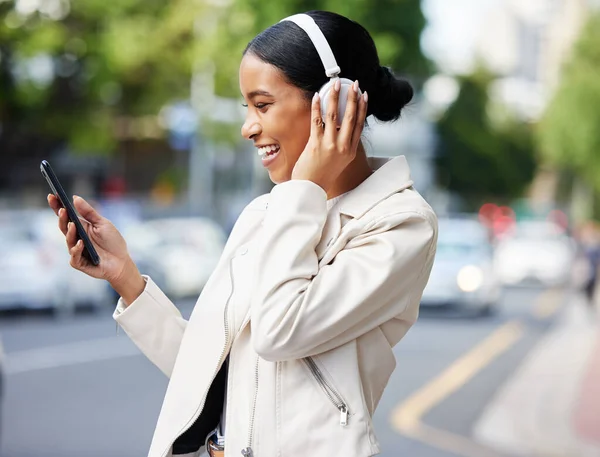 Happy city girl with phone and headphones on video call while walking relax in the street to work or home. Black woman or student laughing at joke, meme or online video while on travel to a location.