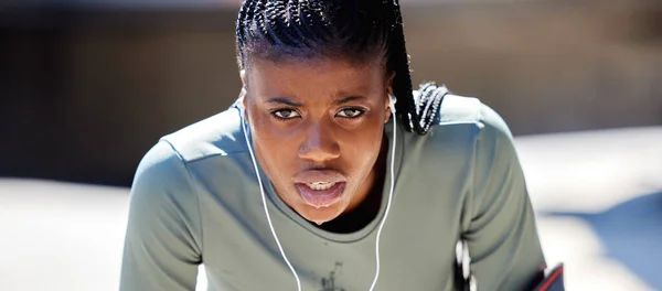 Runner, workout and exercise athlete tired after running or training for a marathon with earphone. Health, wellness and motivation or healthy and strong fitness black woman relax after sports cardio.