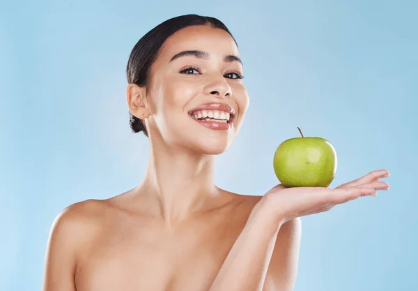 Health, food and apple diet with happy woman holding fruit against blue background. Portrait of a young female excited by weight loss and nutrition, showing benefits of healthy, balance lifestyle.