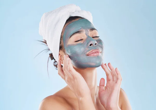 Skincare, body wellness and charcoal face mask for healthy woman skin against blue mockup studio background. Young, happy and beauty cosmetic model with antiaging product for wellbeing and grooming.