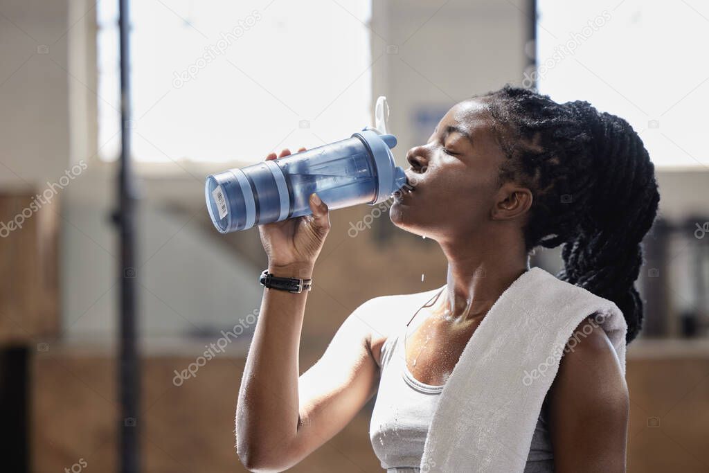 Drinking water and relax after a fitness, workout and exercise training of a woman athlete. Female from Nigeria with sweat done reaching target cardio sports goal at a health, wellness and sports gym.