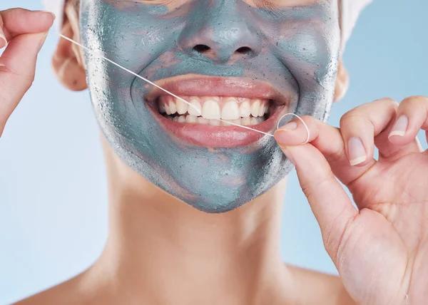 Dental, face mask and woman flossing her teeth for healthy and strong teeth in a studio portrait with a blue background. Girl cleaning her mouth, face and skin with beauty self care and oral hygiene.