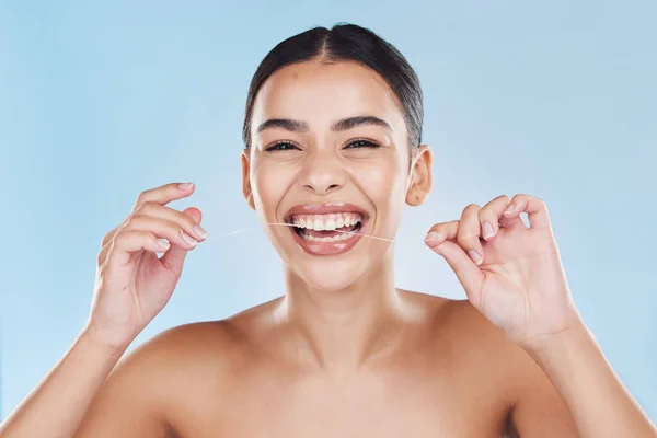 Beauty, teeth and skincare of a woman in dental floss isolated against a blue studio background. Portrait of attractive female flossing for healthy mouth care, tooth and gum hygiene with a big smile