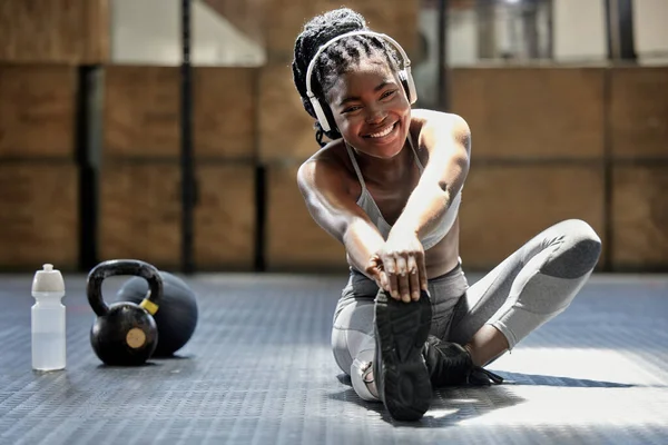 Portrait of woman stretching with music at gym, audio podcast for workout motivation and happy about fitness training on floor at health club. African athlete or sports person doing exercise.