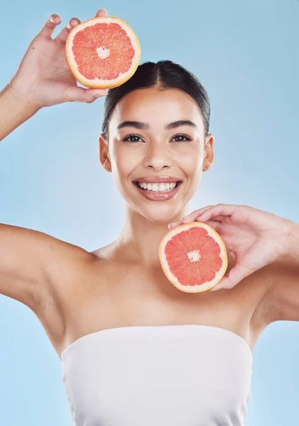Wellness, health and beauty with woman and grapefruit with a smile against a blue background studio. Skincare, nutrition and confident portrait of a young wellbeing female holding fruit.