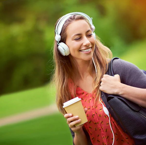 Strolling through the park with her coffee and music. a young woman listening to music while having a coffee on the go