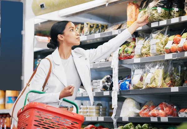 Supermarket, shopping and customer in retail store for vegetable food, groceries or product from shelf. Young woman with basket during inflation price increase, discount or sales choice on grocery.