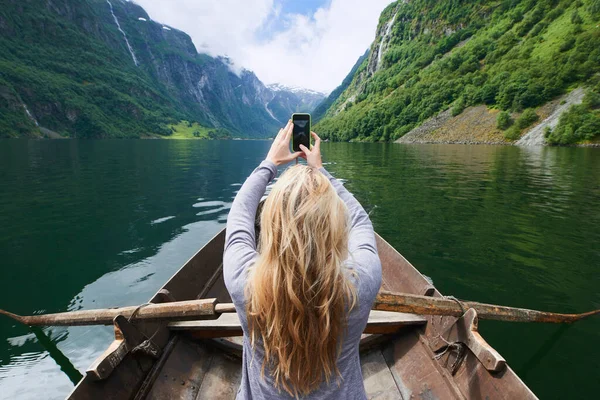 Adventure woman in row boat taking photo on smart phone of beautiful fjord lake for social media.