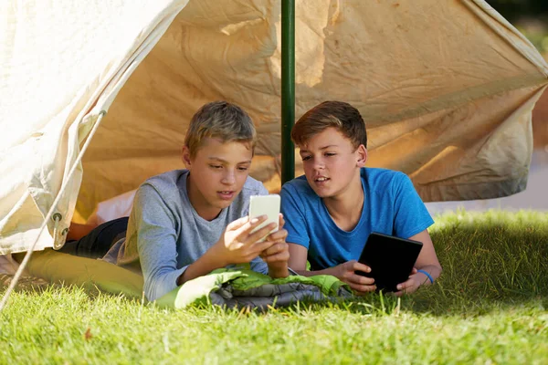 Whoa, thats so cool. A young boy showing his friend something on a cellphone while theyre camping