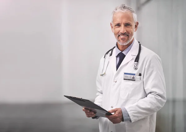 Here to help guide you to good health again. Portrait of a mature male doctor standing with a clipboard in a hospital