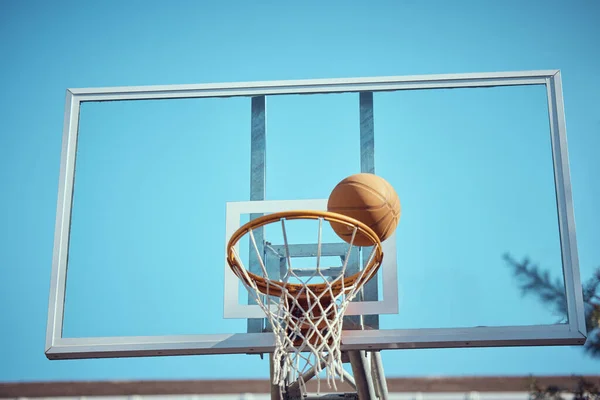 Basketball court, sport and hoop or ring net against a blue sky outside. Exercise, competitive and fun hobby for athletes with a ball on the basket for a goal with copy space or mock up outdoors.