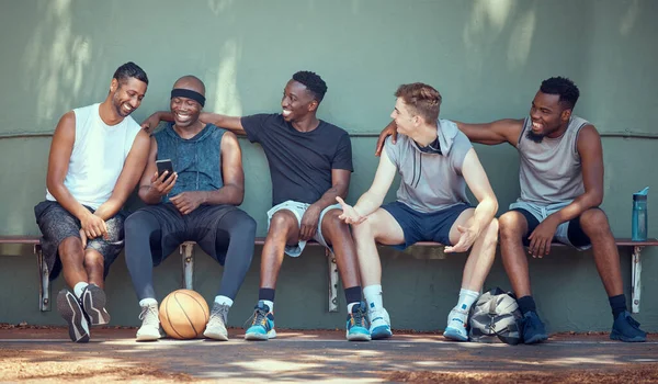 Basketball, sport and friends with a team of men sitting on a bench after training, practice or a game. Teamwork, phone and exercise with a group of basket ball players outside on a sports court.