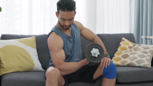 在客厅里 一个男人在沙发上做举重锻炼时的健身 哑铃和二头肌 在沙发上进行二头肌卷曲运动时积极参加力量训练以获得强壮肌肉 — 图库视频影像