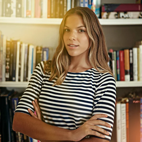 She means business. Portrait of a woman standing in front of bookshelves in her home office