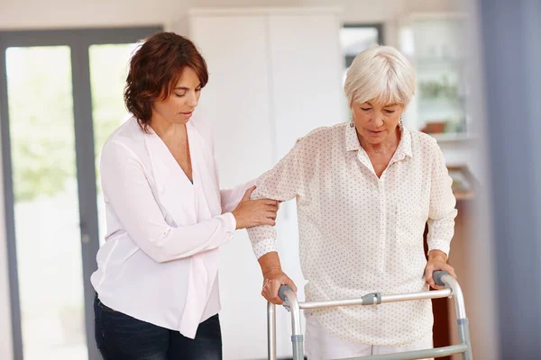 Shes there for her mom in her senior years. a woman assisting her elderly mother with an orthopedic walker