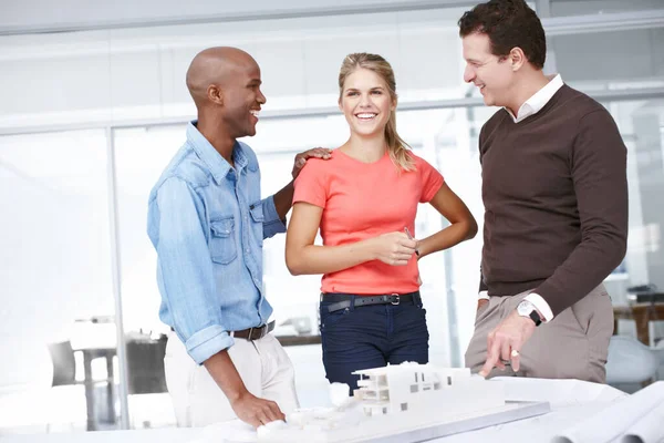 They have a great team dynamic. A group of architects having a discussion as they stand by an architectural model