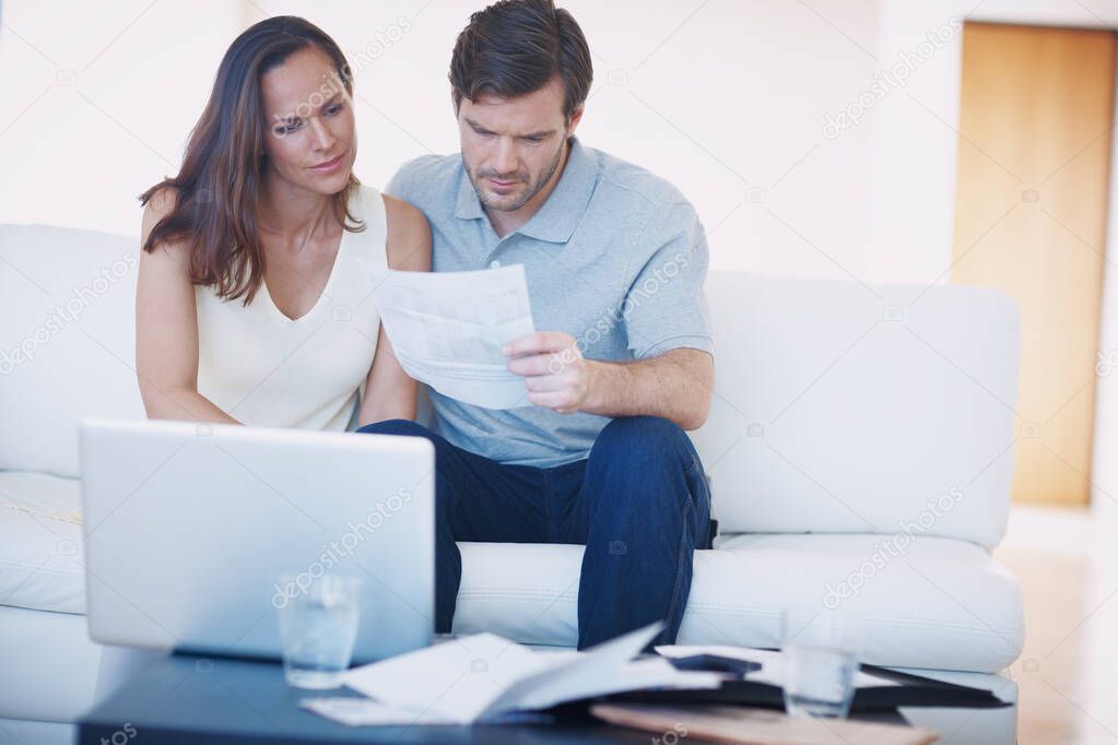 Its budgeting time again...A young couple discussing their home finances and inspecting bills while sitting together in their living room