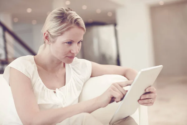在网上看新闻 一个漂亮的金发女人坐在家里用平板电脑 — 图库照片